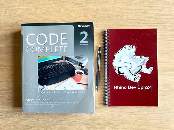 A worn copy of "Code Complete" by Steve McConnell and a notebook from the Rhino Dev Conference in Copenhagen